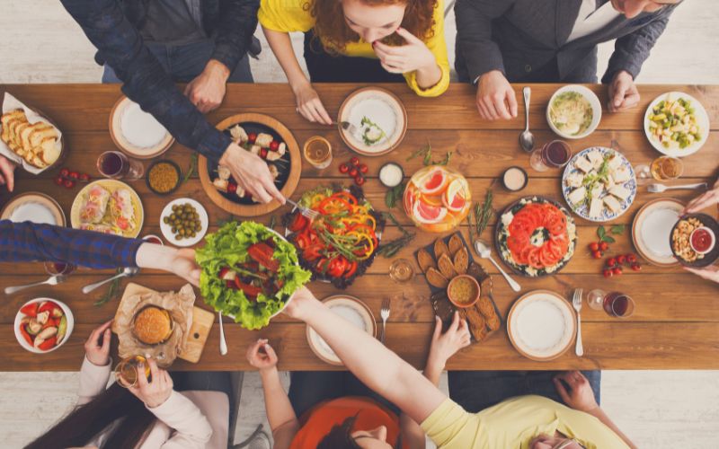 Table vu dans haut, avec pleins de choses à manger et des gens assis autour.