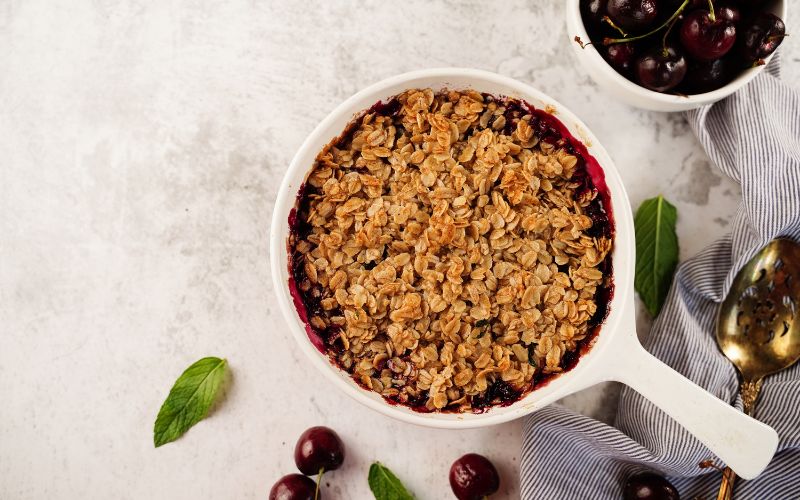 Poêle céramique blanche, avec un crumble fruit rouge dedans, posée sur un plan de travail en granit blanc et gris.