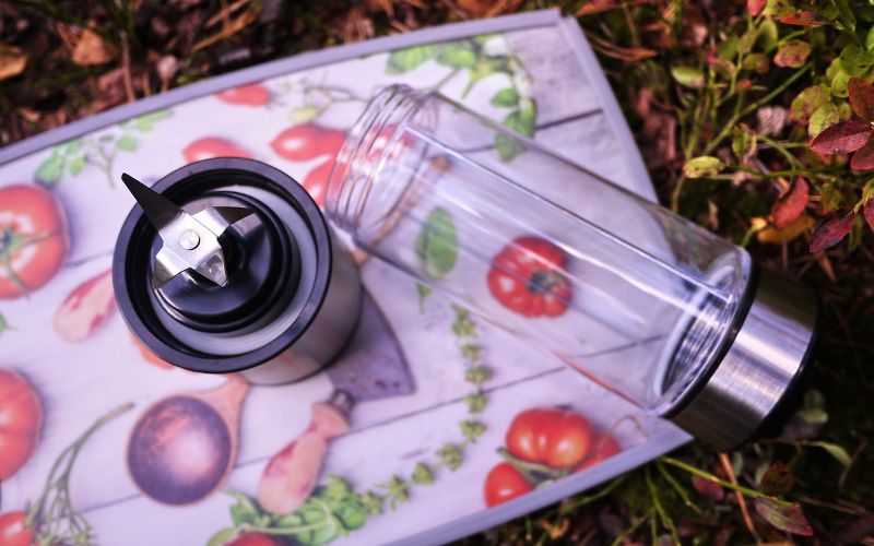 Blender portable ouvert et posé en deux parties sur une planche avec des images de tomates, basilique, cuillère, tomates cerises, etc