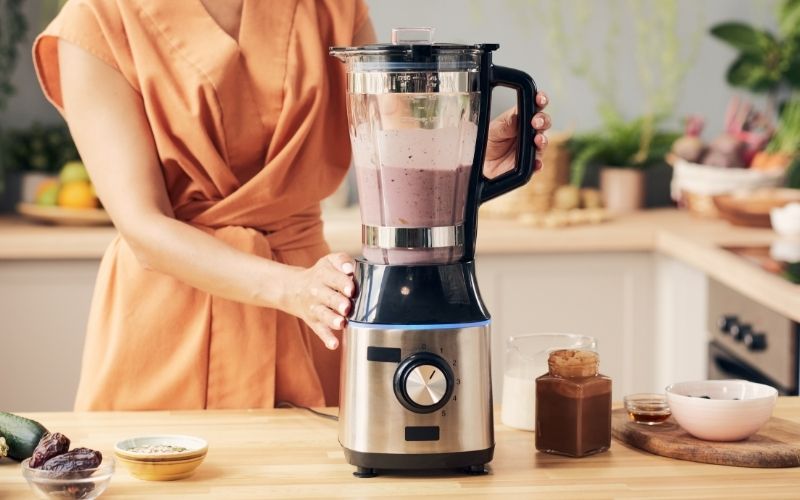 Femme dans sa cuisine, qui utilise un blender pour préparer un repas.