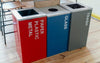 Trois bacs de poubelle de tri installés dans une cuisine. Un rouge, un bleu, un gris.