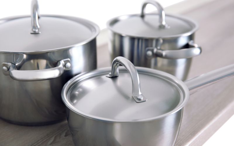 Lot de trois casseroles en inox, deux avec des poignées et une avec un manche, chacune ont un couvercle inox