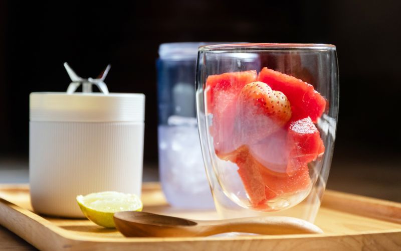 Blender portable blanc à côté d'un verre avec des fraises à l'intérieur.