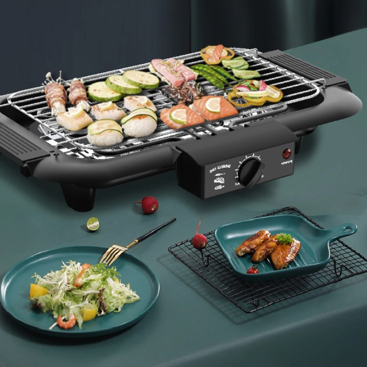 Grill Electrique Portable d'Intérieur Sans Fumée, de couleur noire, positionné sur une table avec des aliments dessus.